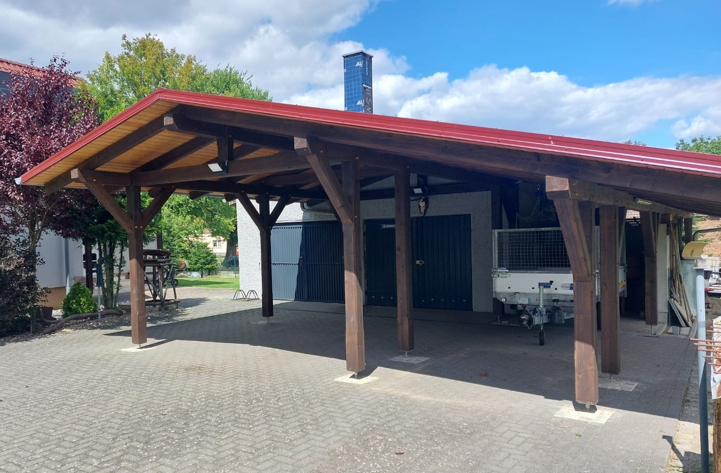 Holz-Carport mit rotem Dach vor einer Garagenzeile
