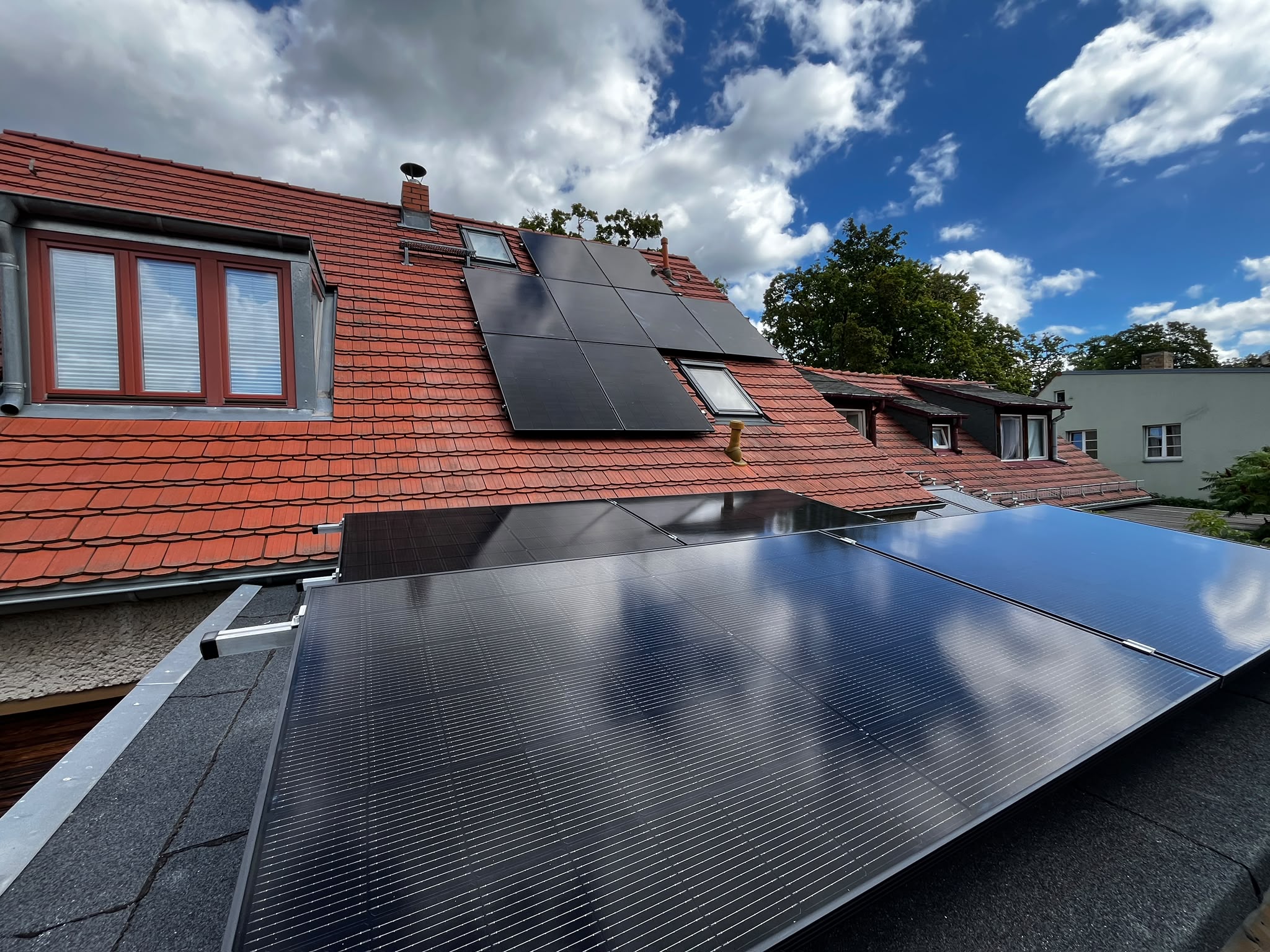 Photovoltaikmodule auf dem Flachdach und dem Ziegeldach eines Wohnhauses