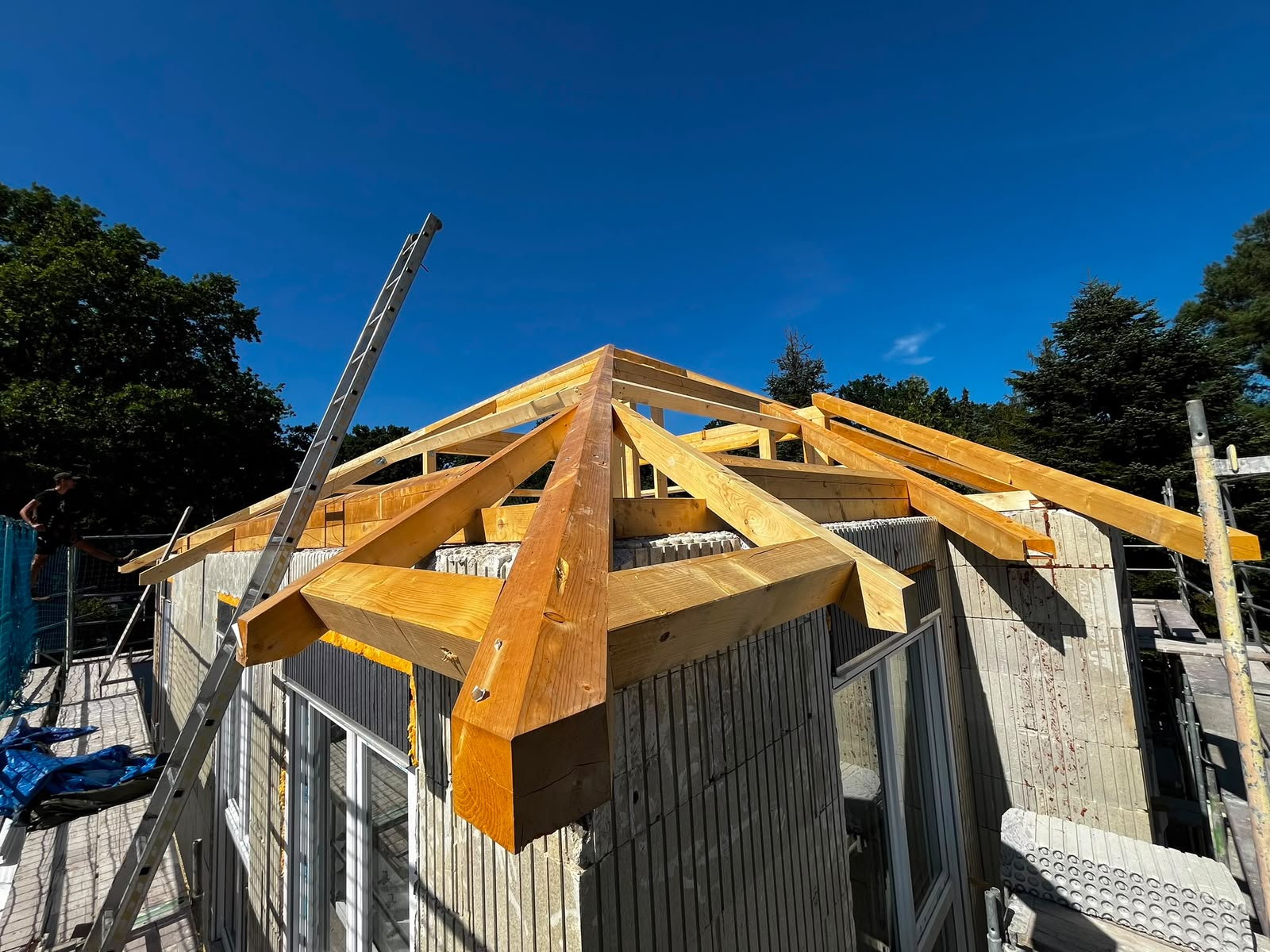 Neuer Walmdach-Dachstuhl aus Holzsparren im Rohbau unter blauem Himmel